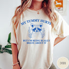 Comfort Colors tee in Ivory featuring line art style raccoon graphic with My Tummy Hurts text design