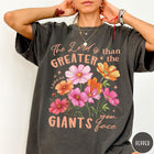 Comfort Colors tee in Pepper featuring floral Bible verse graphic design with 1 John 4:4 scripture text