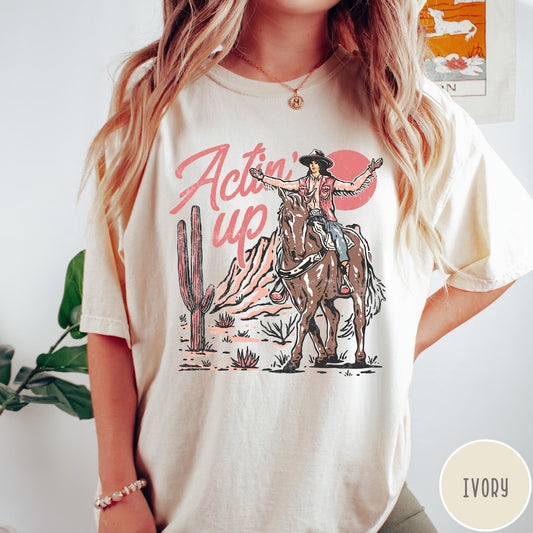 Comfort Colors tee in Ivory featuring western style graphic of a cowgirl riding a horse in the desert
