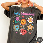 Comfort Colors tee in Pepper featuring retro mascot design with daily affirmations and colorful cartoon characters