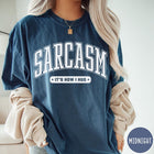 Comfort Colors tee in Midnight featuring collegiate style text reading Sarcasm It's How I Hug
