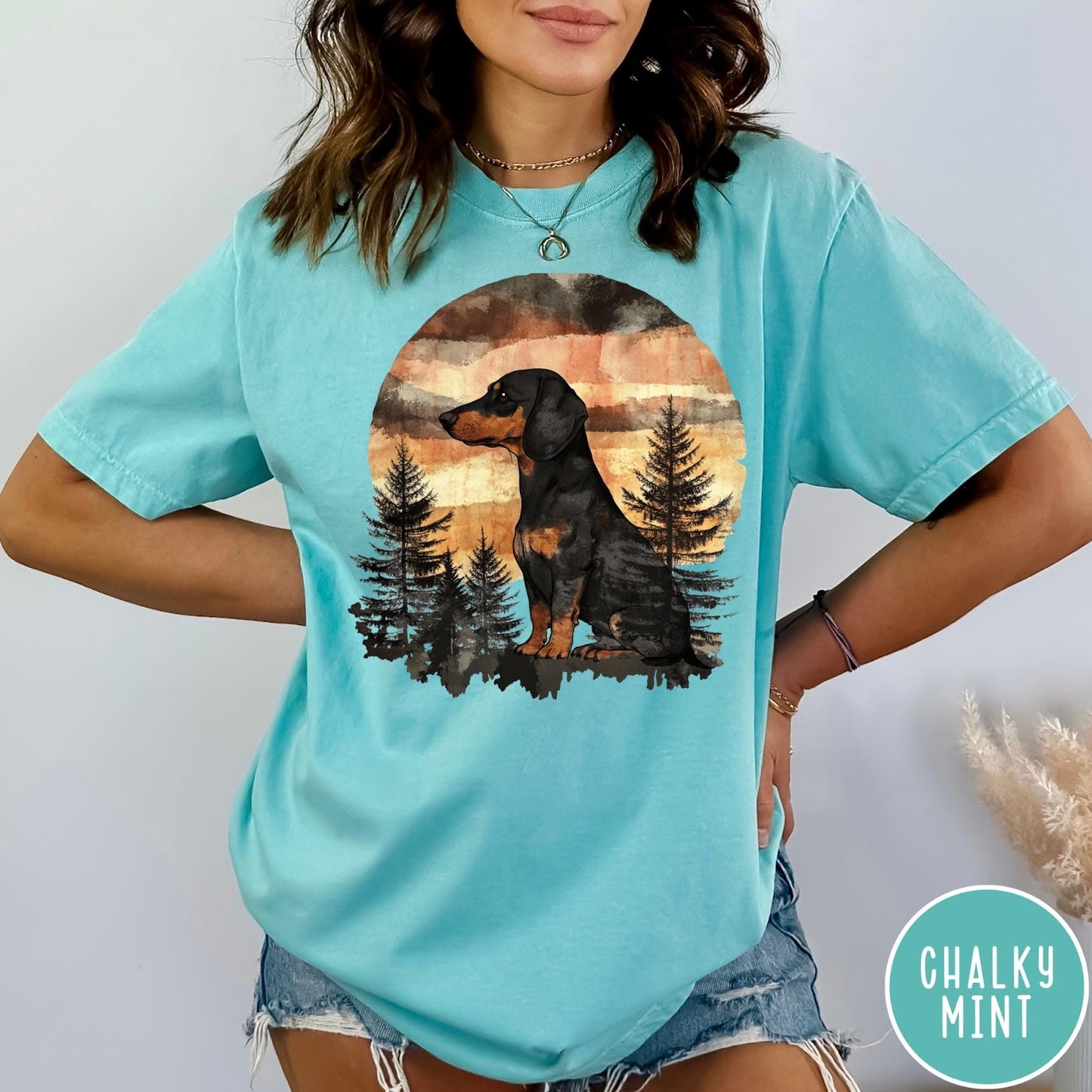 Comfort Colors tee in Chalky Mint featuring vintage style graphic of a dachshund sitting in a forest sunset