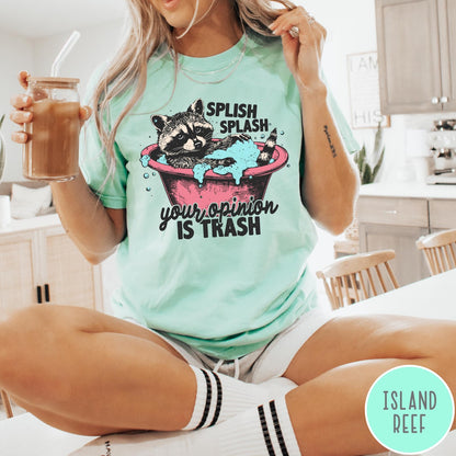 Comfort Colors tee in Island Reef featuring illustrative graphic of a raccoon sitting in a pink bathtub