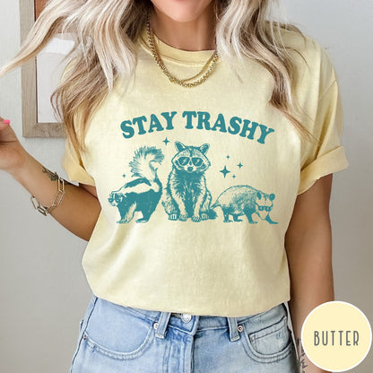 Comfort Colors tee in Butter featuring graphic style raccoon, skunk, and opossum wearing sunglasses with Stay Trashy text