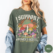 Comfort Colors tee in Moss featuring retro style graphic with mushrooms, flowers, and sun with inspirational text
