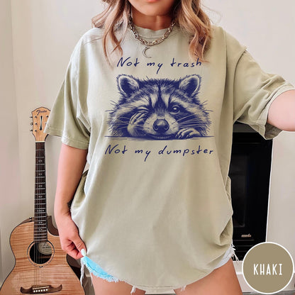 Comfort Colors tee in Khaki featuring graphic illustration of a winking raccoon with text Not My Trash
