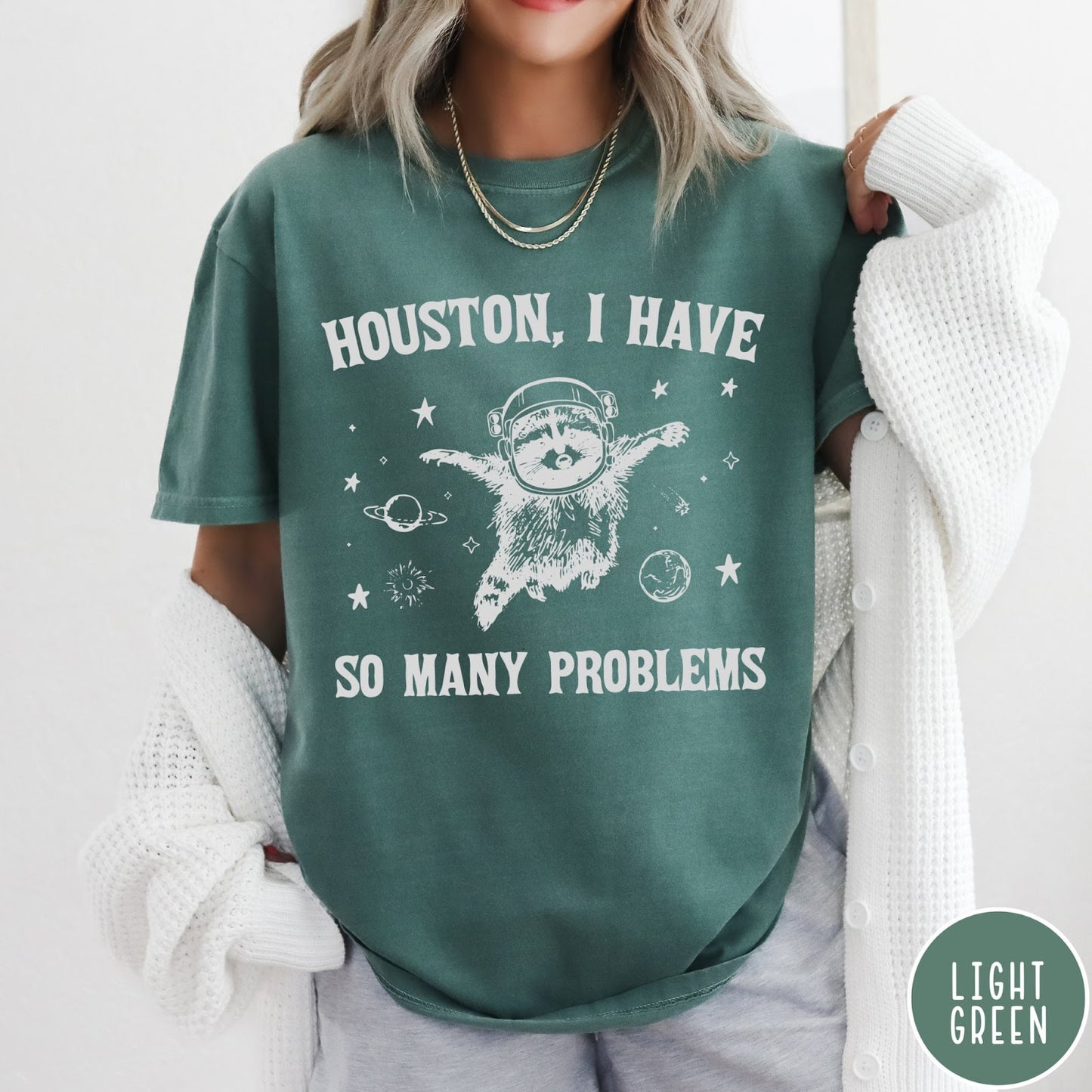 Comfort Colors tee in Light Green featuring space style graphic of a raccoon wearing an astronaut helmet floating