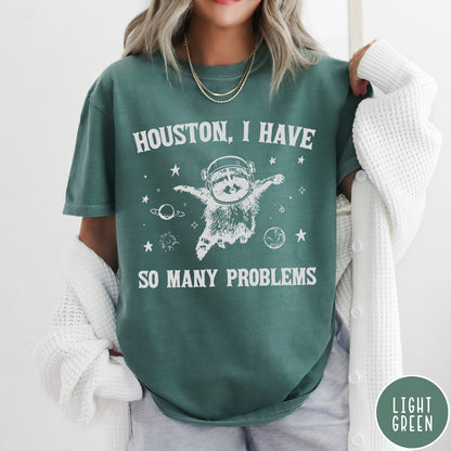 Comfort Colors tee in Light Green featuring space style graphic of a raccoon wearing an astronaut helmet floating