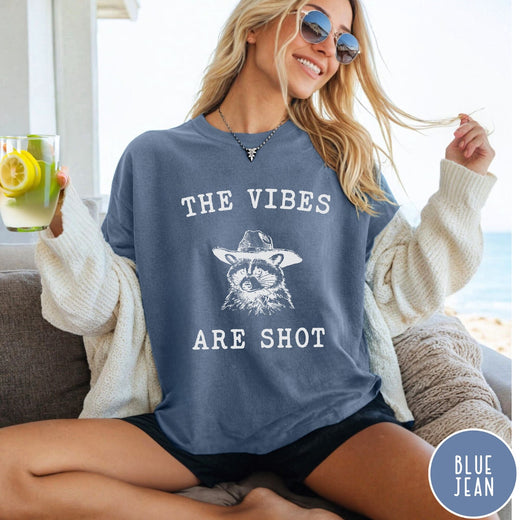 Comfort Colors tee in Blue Jean featuring graphic style raccoon wearing a cowboy hat and text The Vibes Are Shot