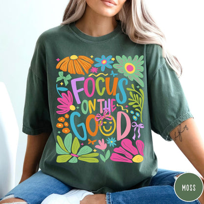 Comfort Colors tee in Moss featuring positivity typography and floral collage graphic with a smiley face.