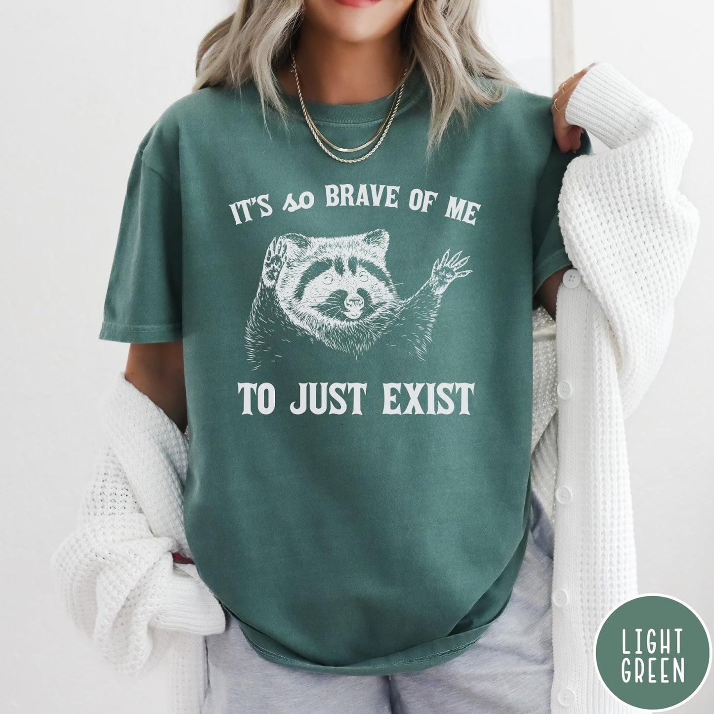 Comfort Colors tee in Light Green featuring illustrative raccoon graphic with text It's So Brave Of Me To Just Exist