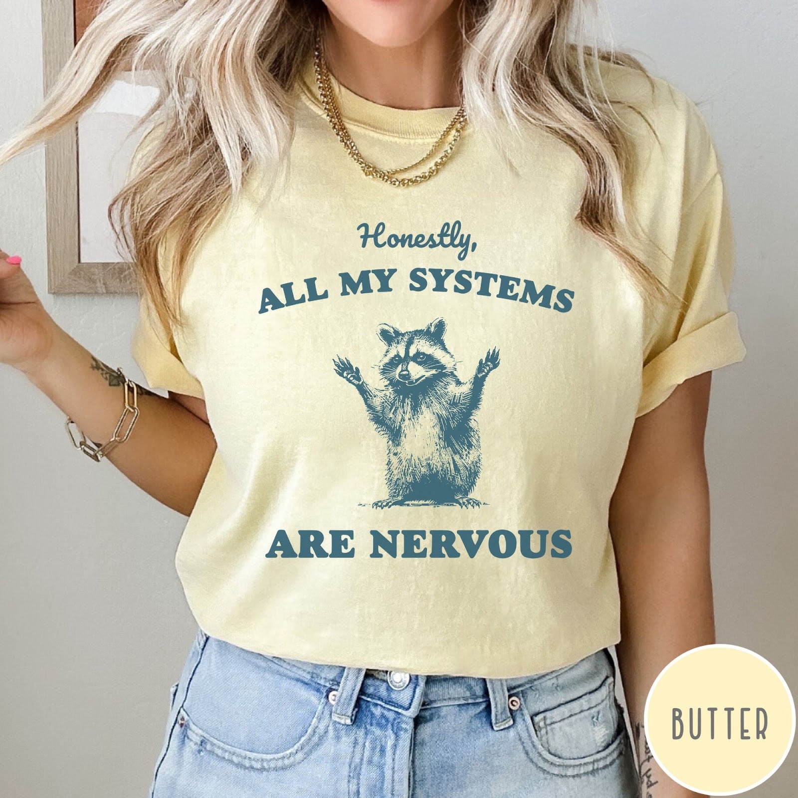 Comfort Colors tee in Butter featuring graphic illustration of a nervous raccoon with arms raised in air