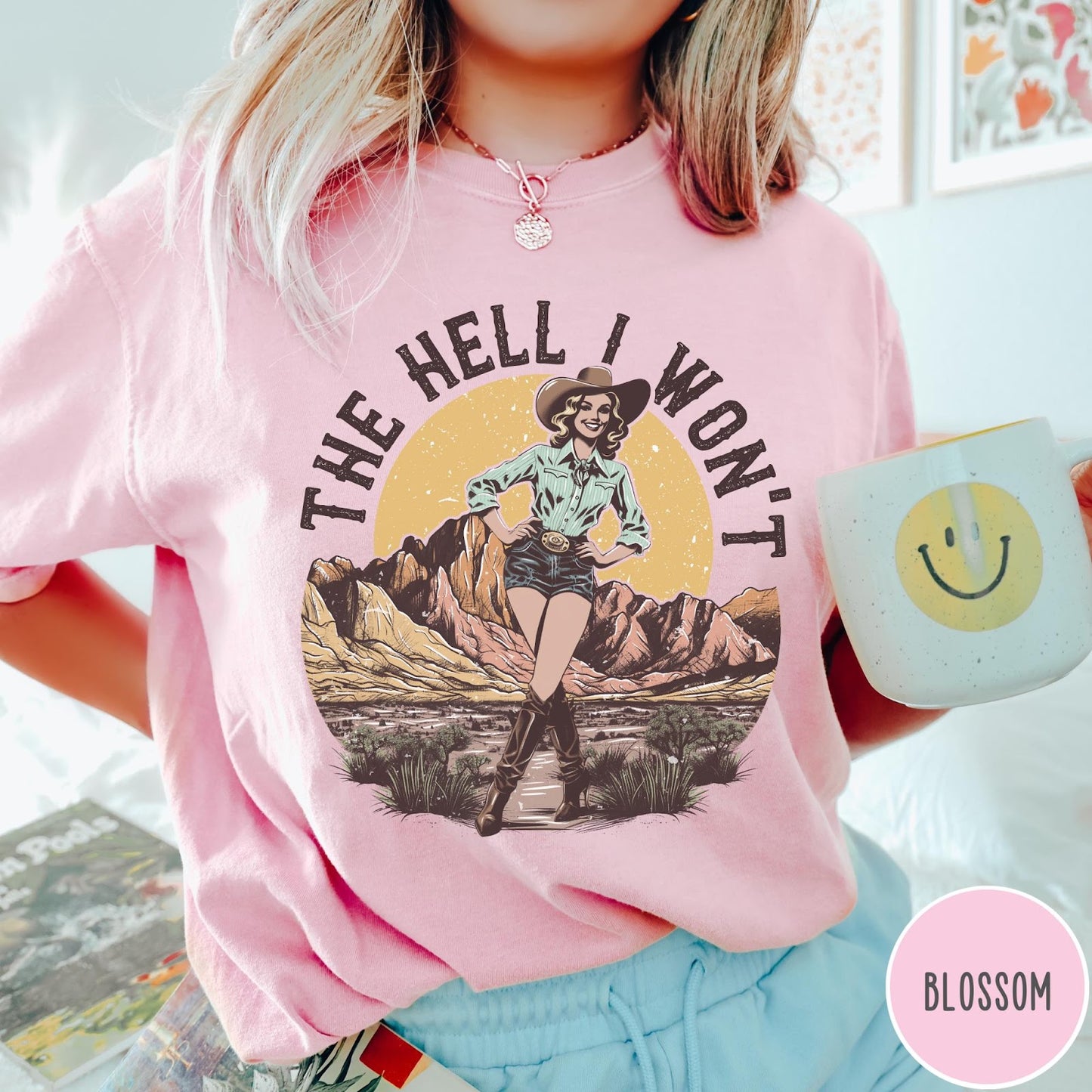 Comfort Colors tee in Blossom featuring western graphic design of a cowgirl standing in front of mountains.