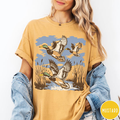 Comfort Colors tee in Mustard featuring vintage style mallard ducks flying over a marshy pond graphic