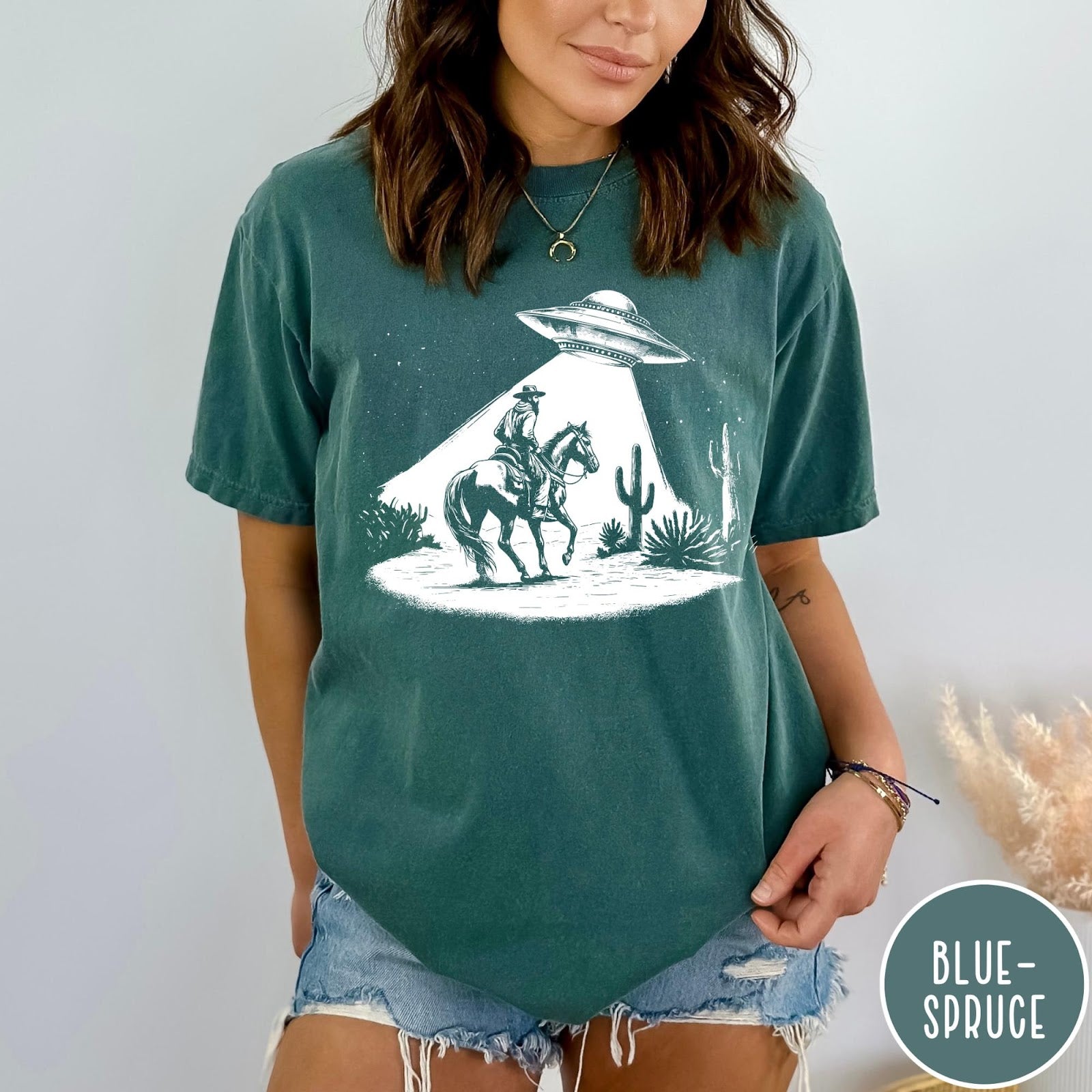 Comfort Colors tee in Blue Spruce featuring western graphic style cowboy on horseback being abducted by a UFO
