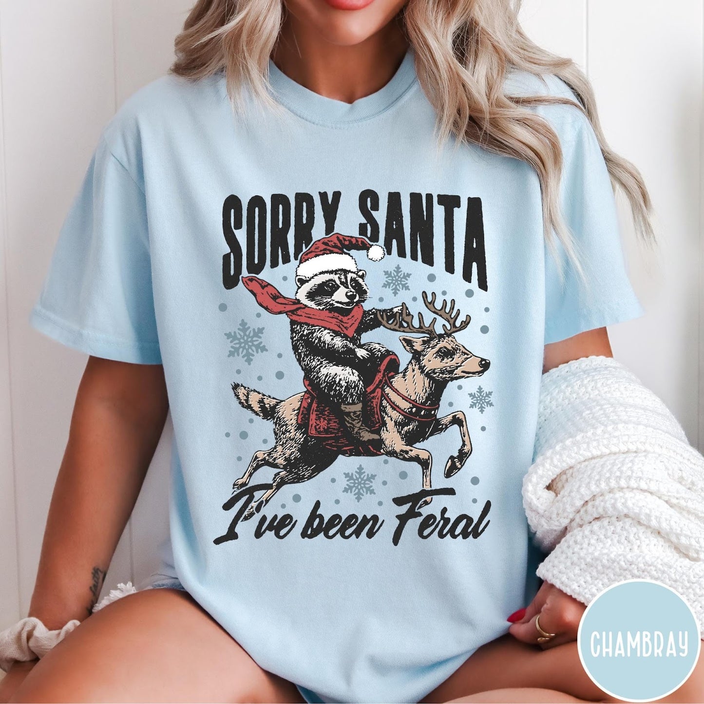 Comfort Colors tee in Chambray featuring festive graphic of a raccoon wearing a Santa hat riding a reindeer