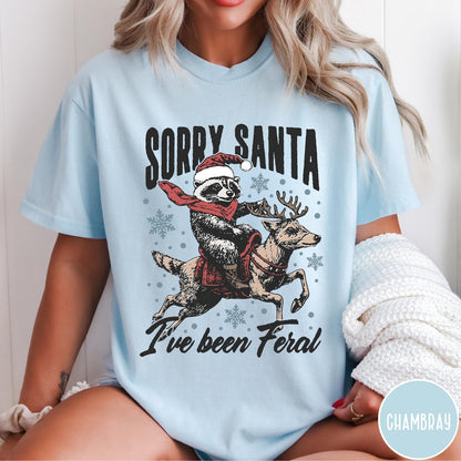 Comfort Colors tee in Chambray featuring festive graphic of a raccoon wearing a Santa hat riding a reindeer