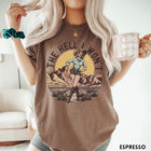 Comfort Colors tee in Espresso featuring western graphic design of a cowgirl standing in front of mountains.