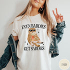 Comfort Colors tee in Ivory featuring cat graphic with sunglasses and popcorn, text Even Baddies Get Saddies