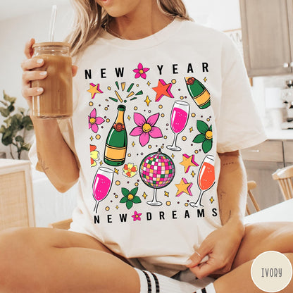 Comfort Colors tee in Ivory featuring New Year celebration graphic with champagne bottles, glasses, and disco ball