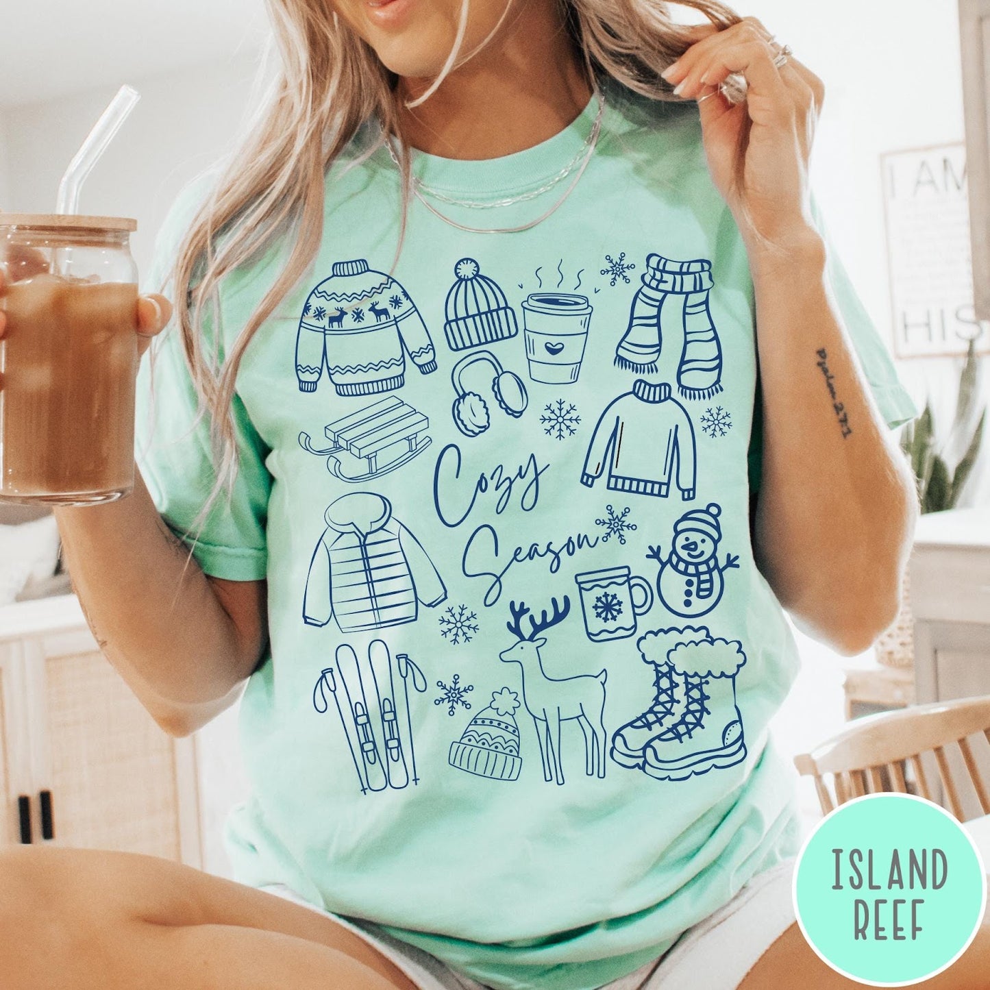 Comfort Colors tee in Island Reef featuring winter activities graphic with sweaters, sled, snowman, and seasonal items.