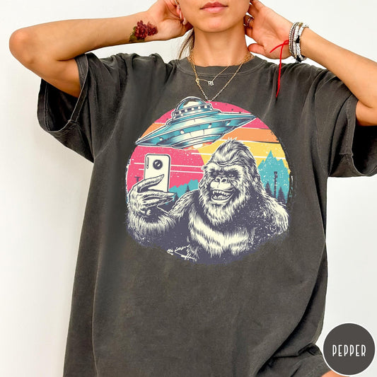 Comfort Colors tee in Pepper featuring retro graphic design of Bigfoot taking a selfie with a UFO