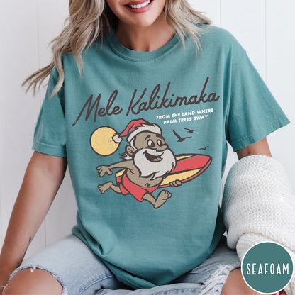 Comfort Colors tee in Seafoam featuring vintage style graphic of a surfing Santa Claus on vacation