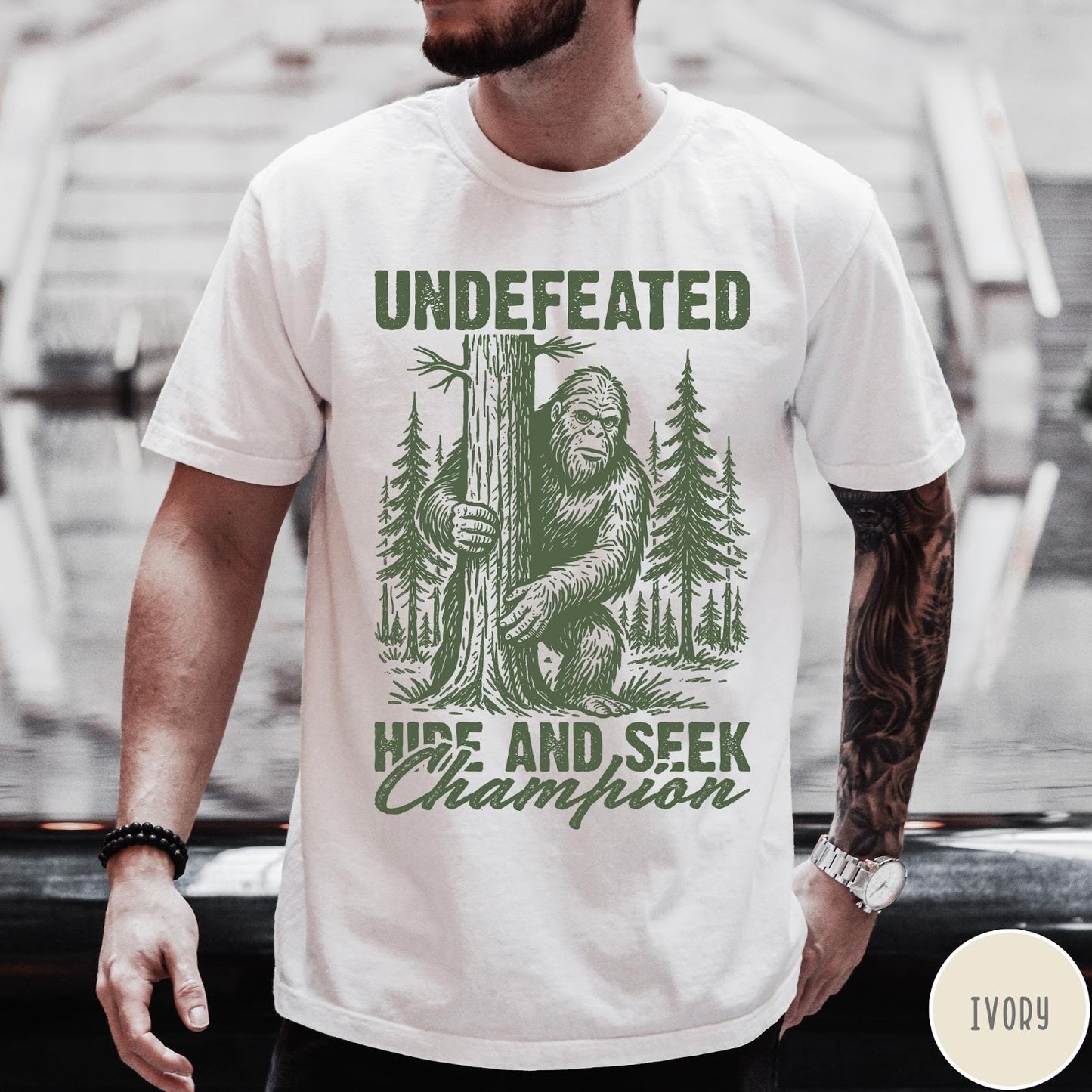 Comfort Colors tee in Ivory featuring vintage style Bigfoot graphic hiding behind a tree in the forest