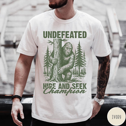 Comfort Colors tee in Ivory featuring vintage style Bigfoot graphic hiding behind a tree in the forest