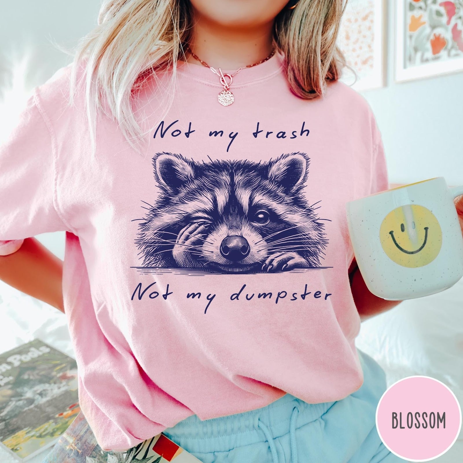 Comfort Colors tee in Blossom featuring graphic illustration of a winking raccoon with text Not My Trash