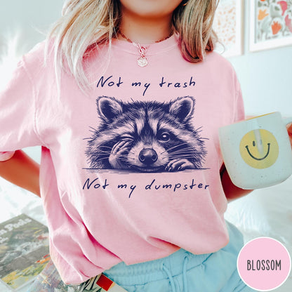 Comfort Colors tee in Blossom featuring graphic illustration of a winking raccoon with text Not My Trash