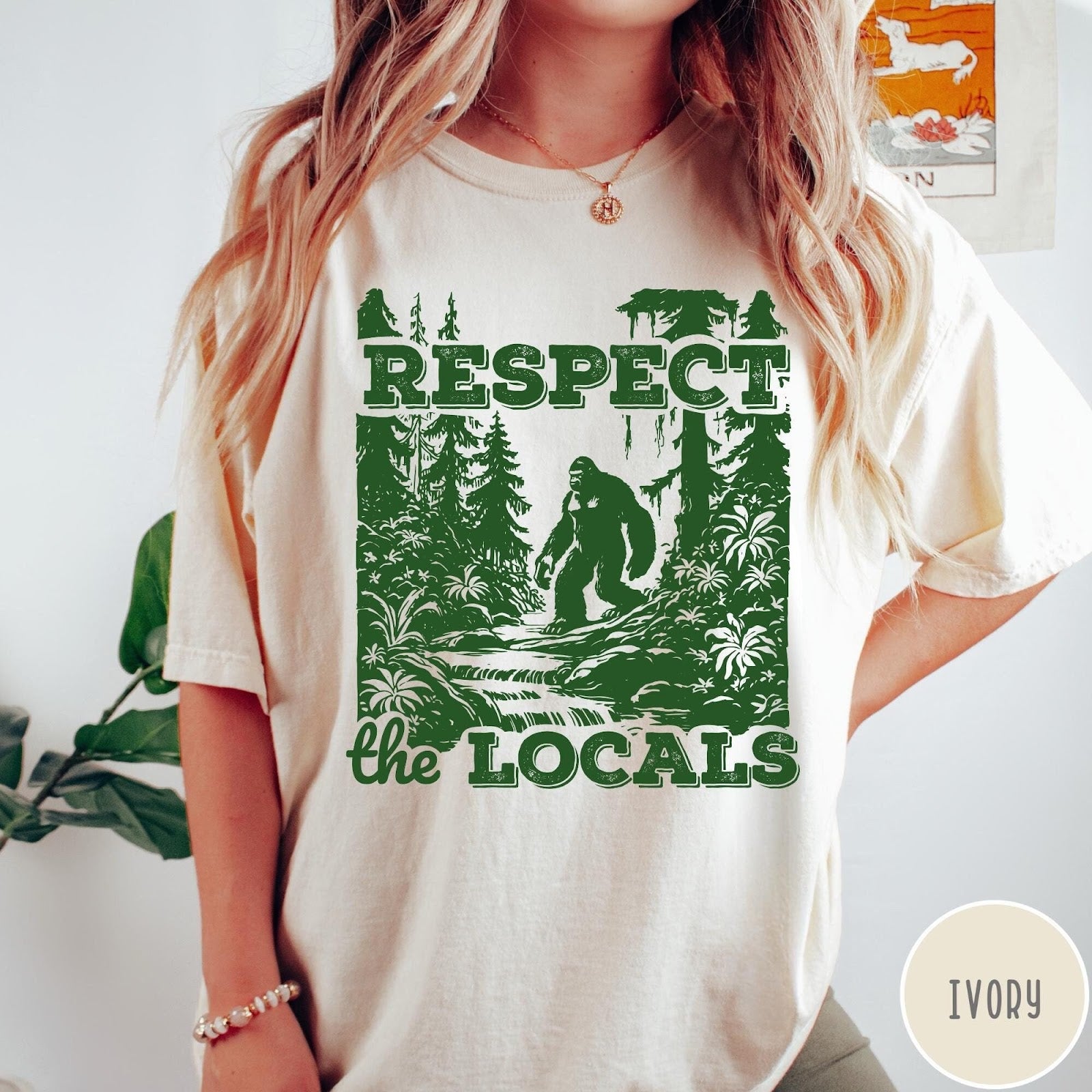 Comfort Colors tee in Ivory featuring vintage style graphic of Bigfoot walking through a forest by a river
