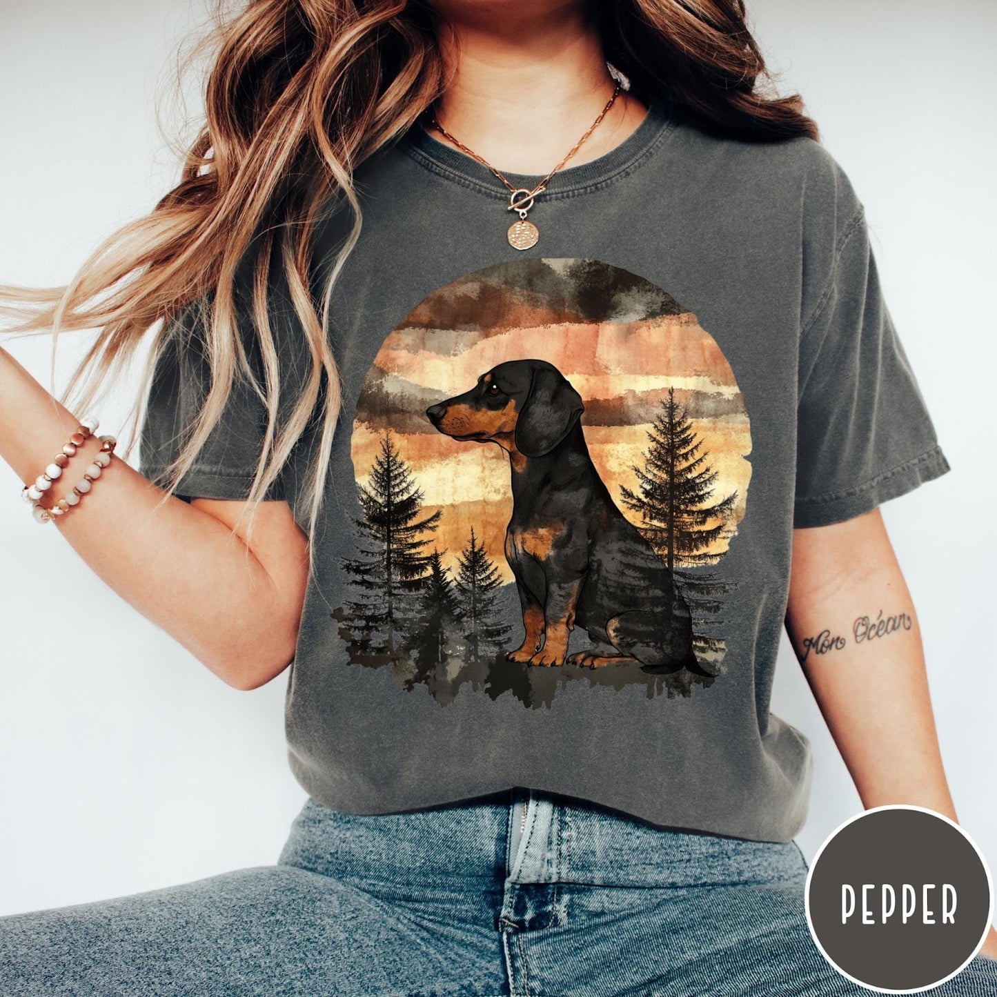 Comfort Colors tee in Pepper featuring vintage style graphic of a dachshund sitting in a forest sunset