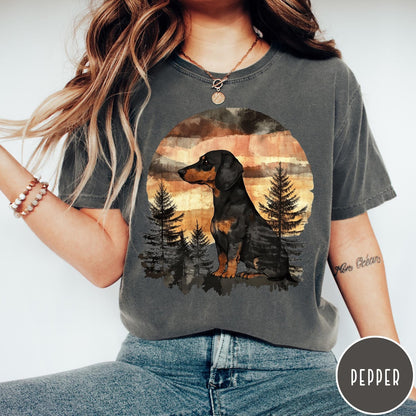 Comfort Colors tee in Pepper featuring vintage style graphic of a dachshund sitting in a forest sunset
