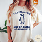 Comfort Colors tee in Ivory featuring penguin graphic with text I am really cold but I am brave
