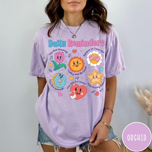 Comfort Colors tee in Orchid featuring retro mascot design with daily affirmations and colorful cartoon characters