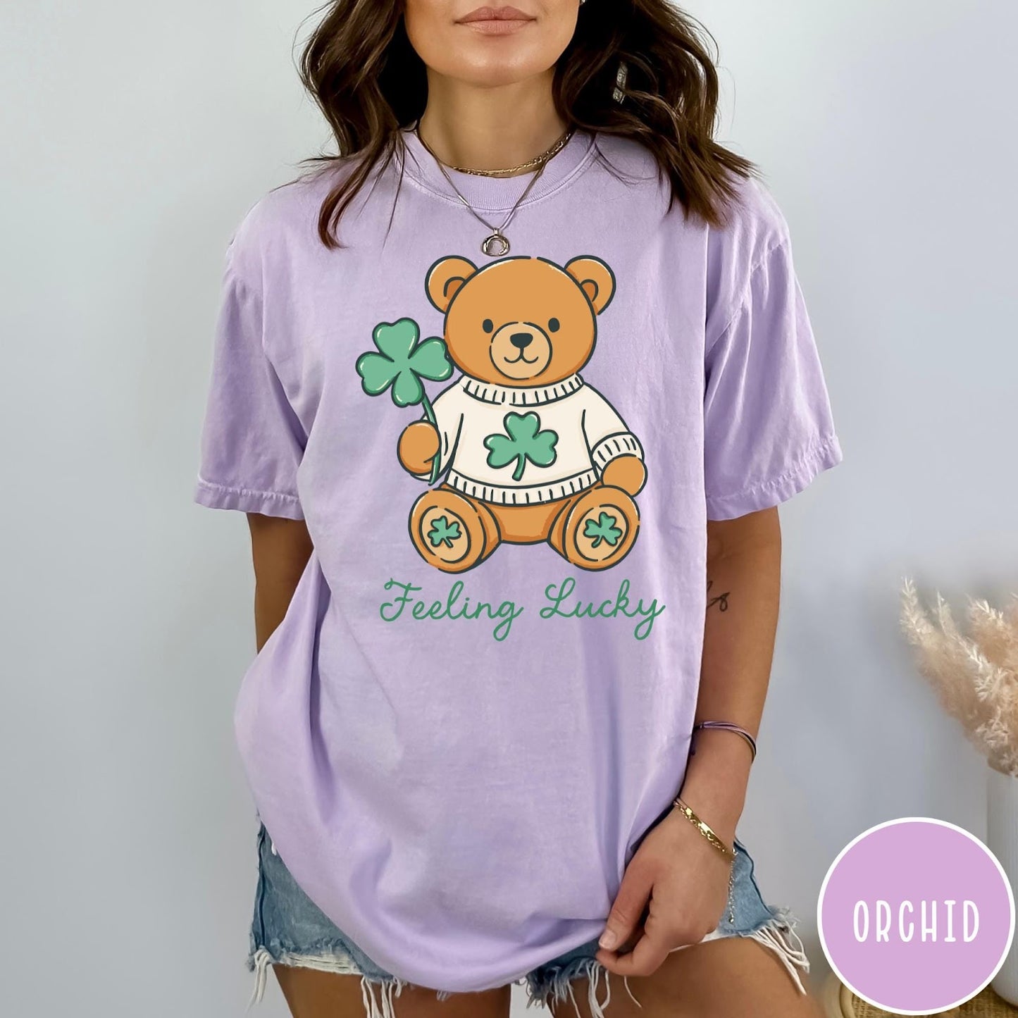 Comfort Colors tee in Orchid featuring illustrated teddy bear wearing a sweater and holding a four-leaf clover