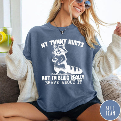 Comfort Colors tee in Blue Jean featuring graphic illustration of a standing raccoon with funny text about being brave