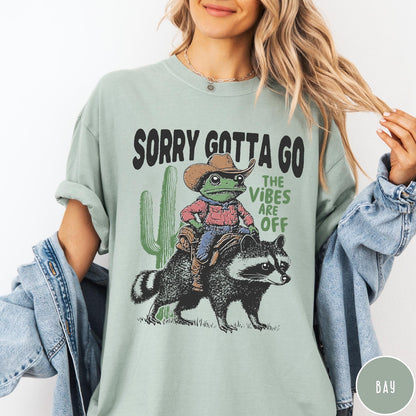Comfort Colors tee in Bay featuring western graphic of a cowboy frog riding a raccoon with cactus