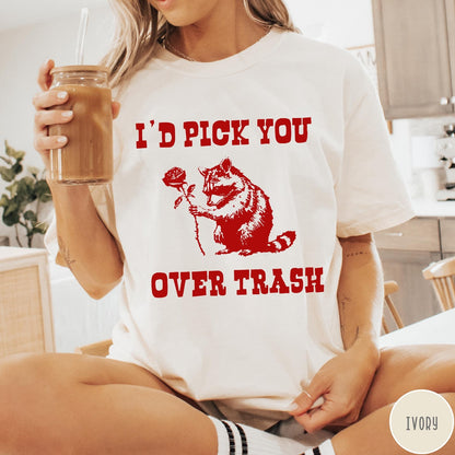 Comfort Colors tee in Ivory featuring a whimsical graphic of a raccoon holding a red rose.