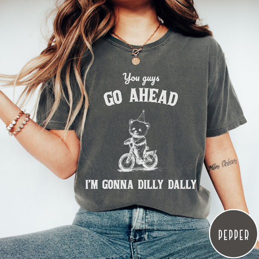 Comfort Colors tee in Pepper featuring illustration style graphic of a bear wearing a party hat riding bicycle