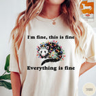 Comfort Colors tee in Ivory featuring graphic illustration of an opossum tangled in colorful Christmas lights