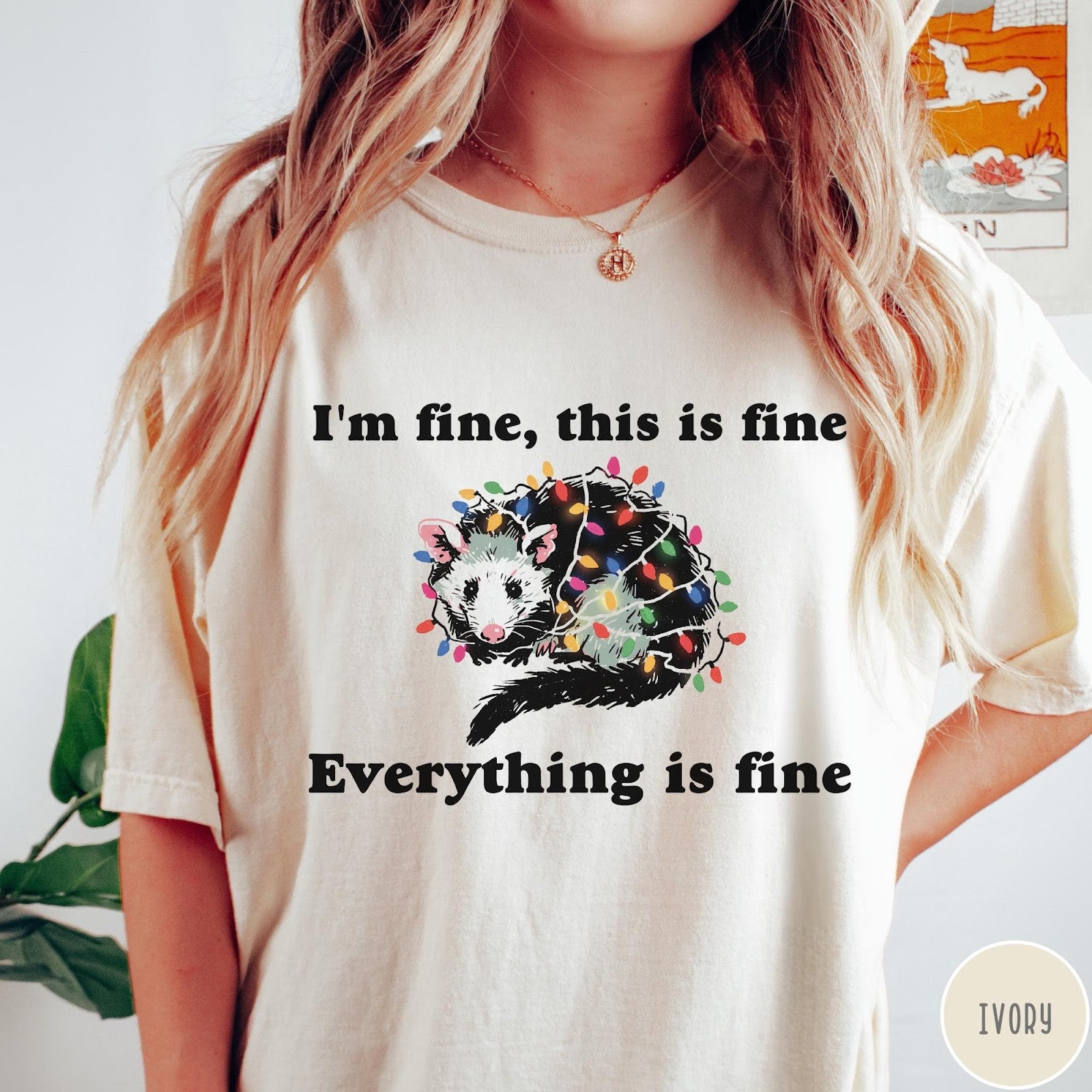 Comfort Colors tee in Ivory featuring graphic illustration of an opossum tangled in colorful Christmas lights