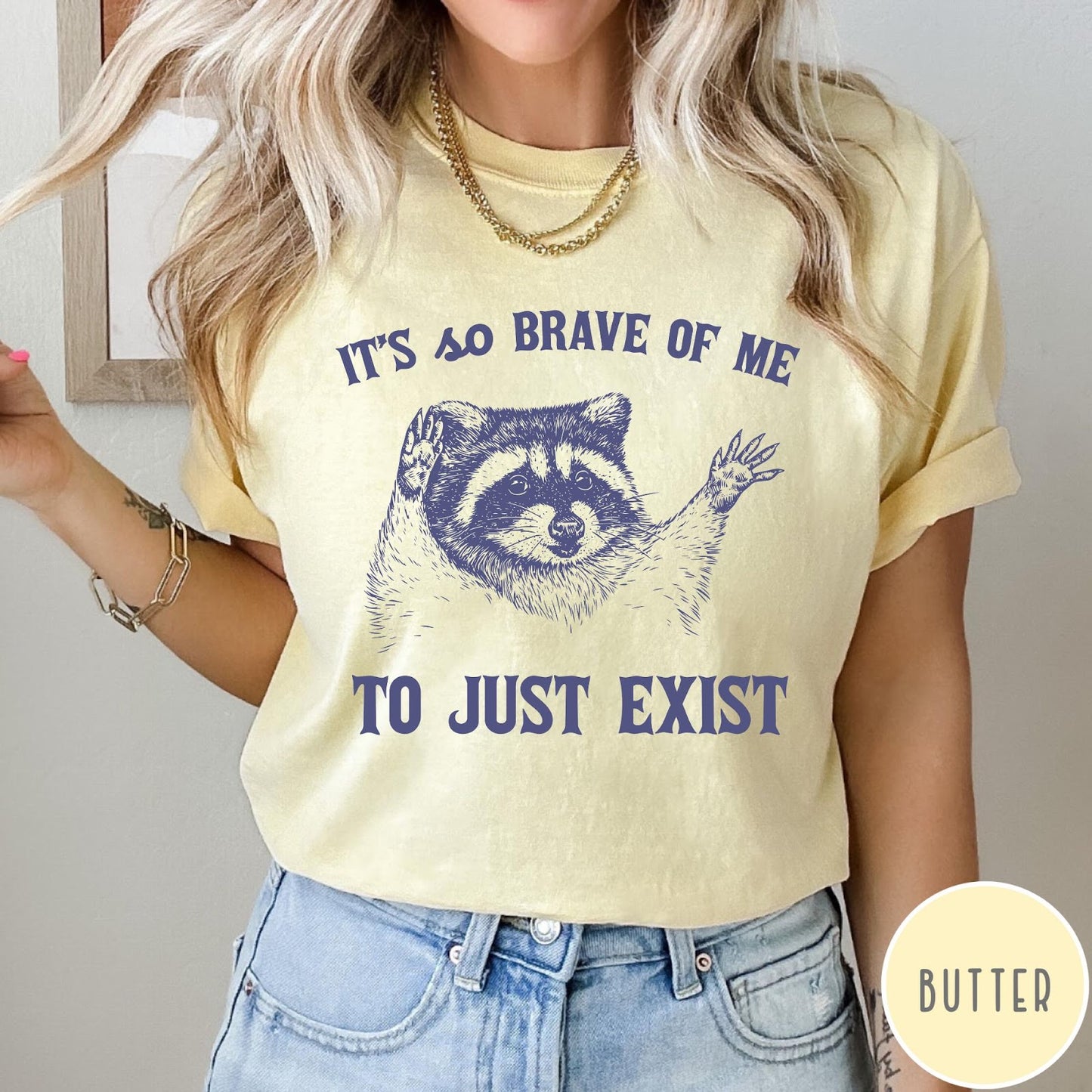Comfort Colors tee in Butter featuring illustrative raccoon graphic with text It's So Brave Of Me To Just Exist