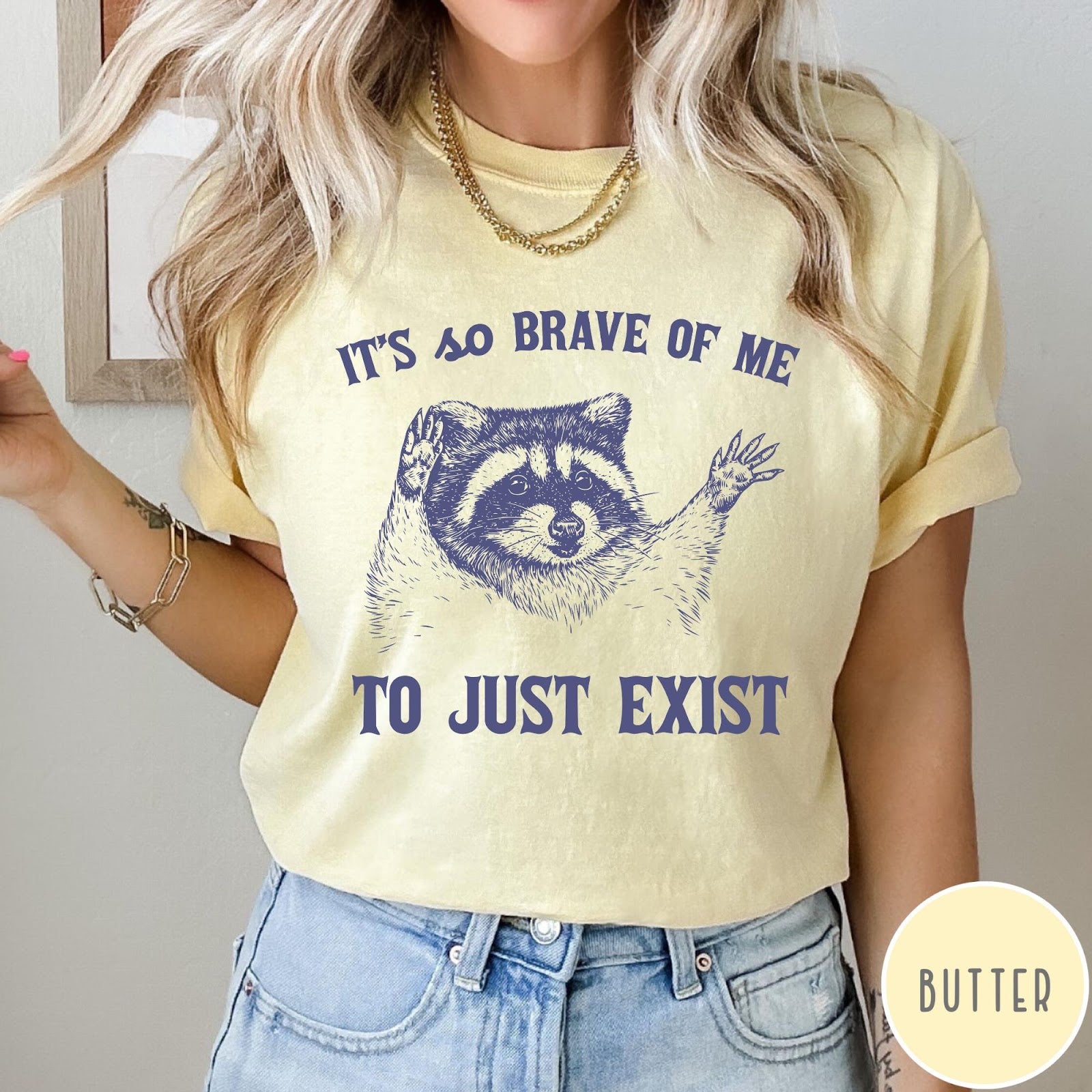 Comfort Colors tee in Butter featuring illustrative raccoon graphic with text It's So Brave Of Me To Just Exist