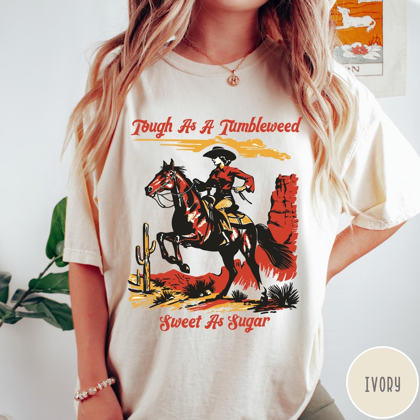 Comfort Colors tee in Ivory featuring western style graphic of a cowgirl riding a horse in desert