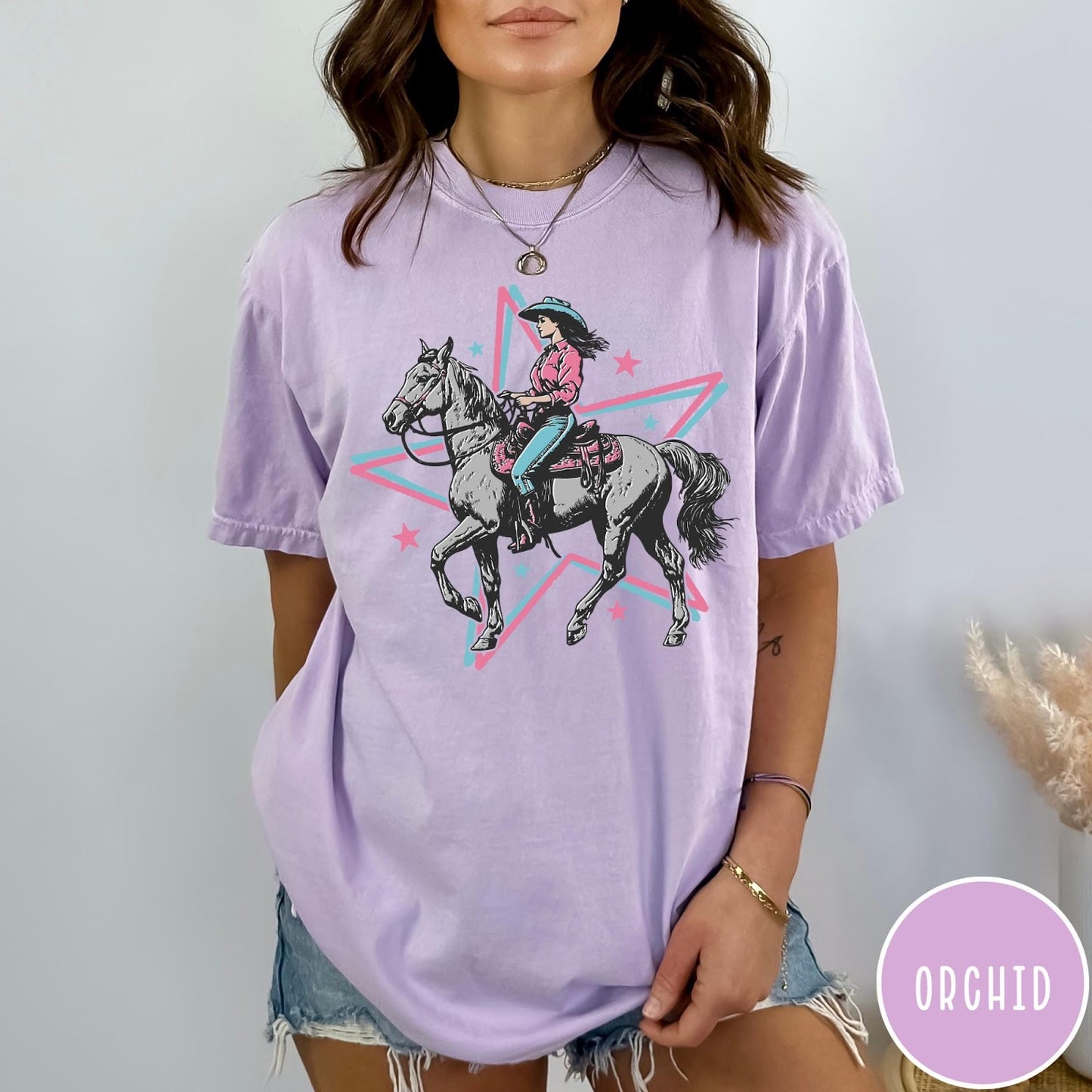 Comfort Colors tee in Orchid featuring retro cowgirl graphic with a woman riding a horse inside a star