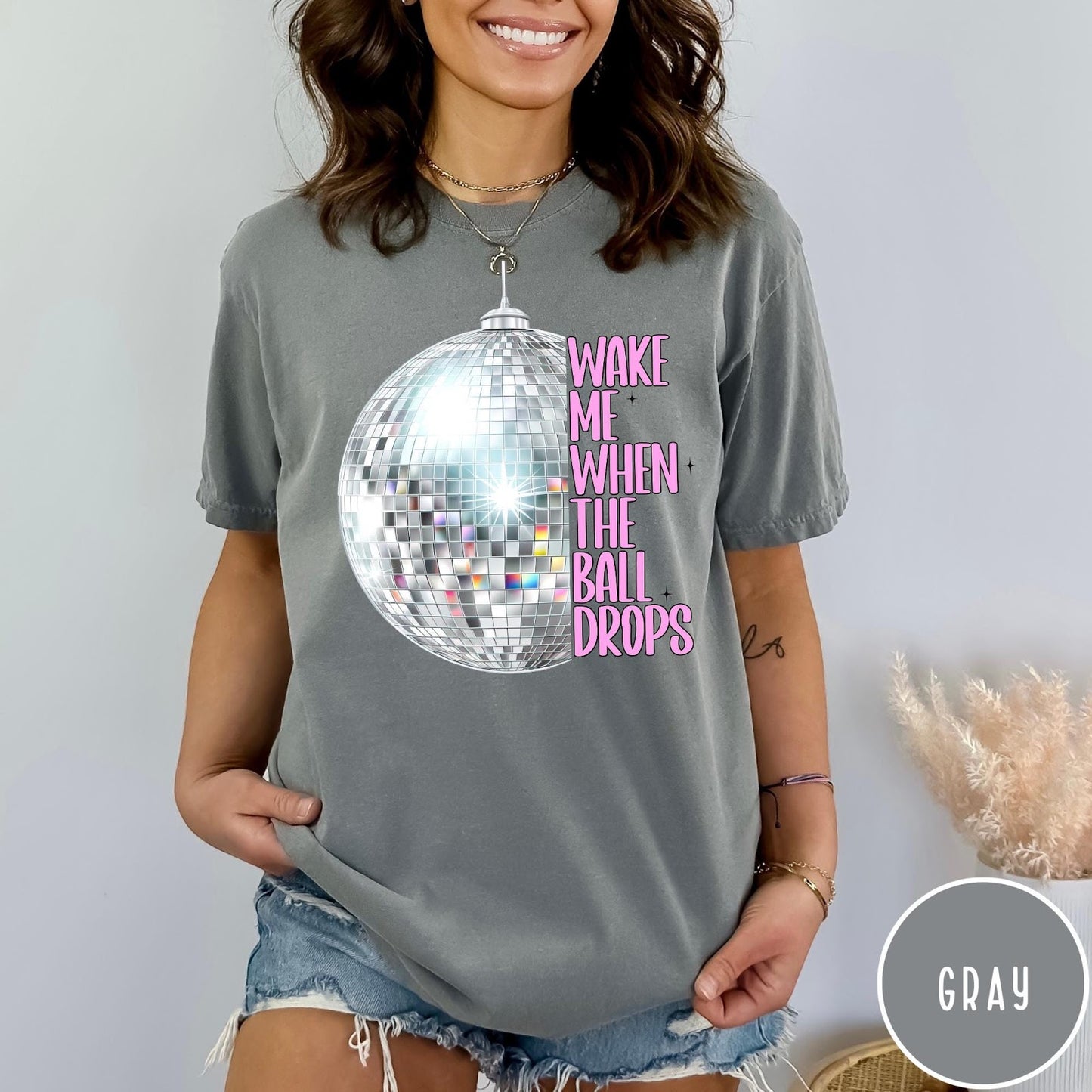 Comfort Colors tee in Gray featuring disco ball graphic and pink text reading Wake Me When The Ball Drops