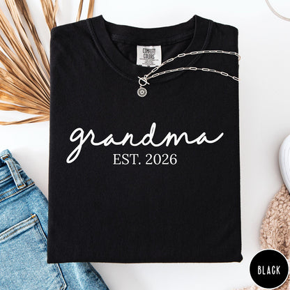 Comfort Colors tee in Black featuring script design Grandma Est. 2026 announcement graphic in white