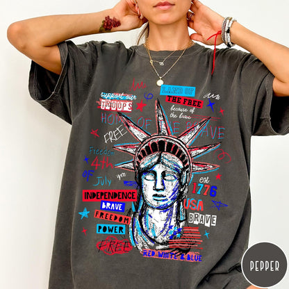 Comfort Colors tee in Pepper featuring grunge style Statue of Liberty graphic with patriotic red and blue text